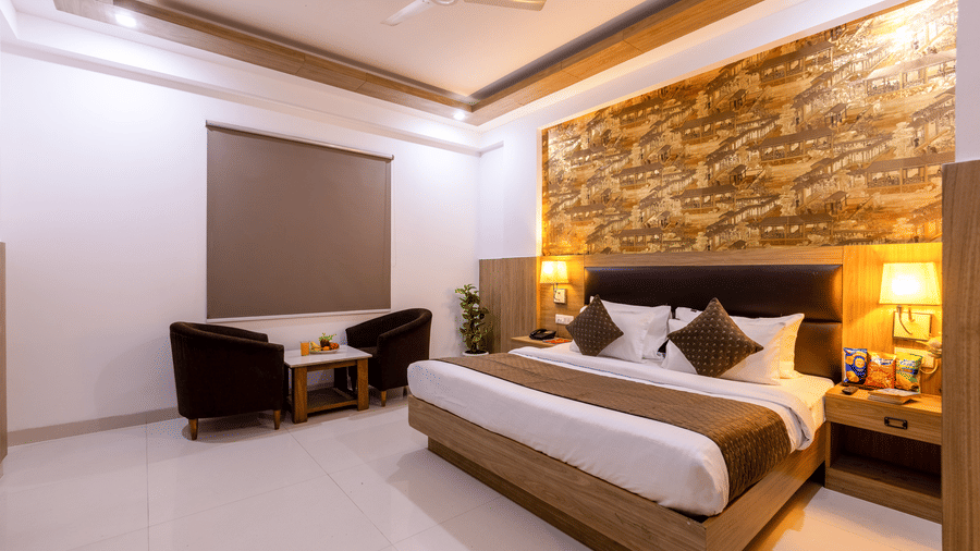 A well-lit Deluxe Room at Hotel Corporate Suites featuring a plush bed against a patterned wall and a seating space next to it