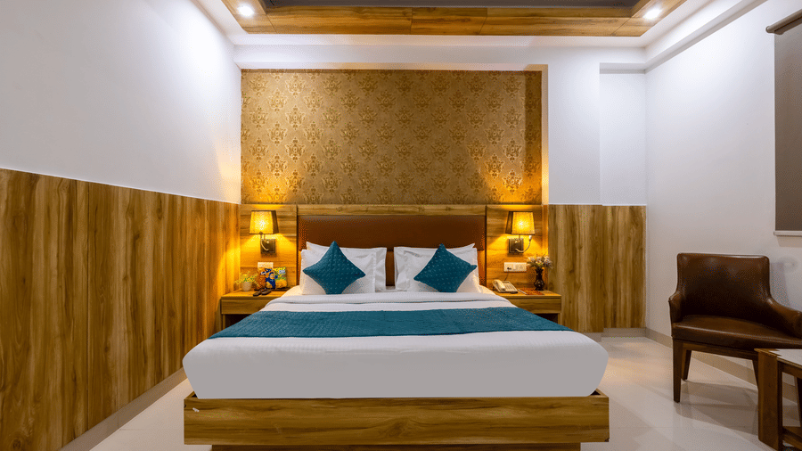 Deluxe Room featuring a central bed with teal cushioning and a seating area with leather chairs under golden lighting at Hotel Corporate Suites