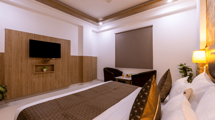 Deluxe Room at Hotel Corporate Suites featuring a bed facing the wall-mounted TV and a seating space next to the window