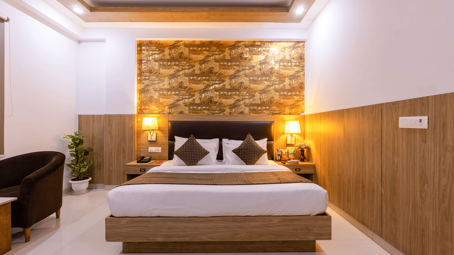 Deluxe Room at Hotel Corporate Suites featuring a plush bed against a patterned wall and lamps lit on both sides of the bed