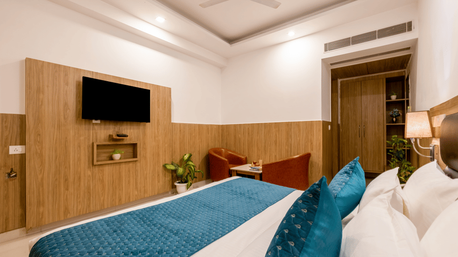 Deluxe Room at Hotel Corporate Suites featuring a plush bed facing the wall-mounted TV and a seating space by the wardrobe