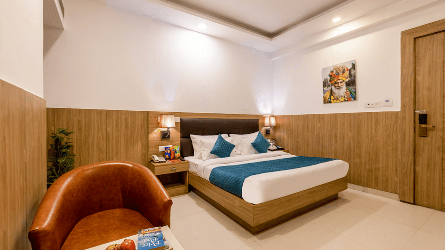 Deluxe Room at Hotel Corporate Suites featuring a bed with lamps lit on both sides and leather chair in front of a coffee table with fruits on it