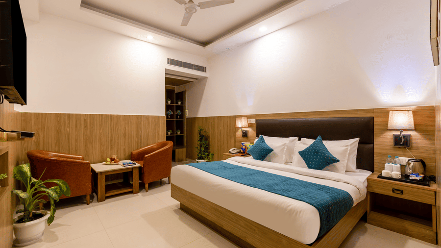Deluxe Room at Hotel Corporate Suites featuring a double bed with lamps lit on both sides over the nightstands and seating space against the wall