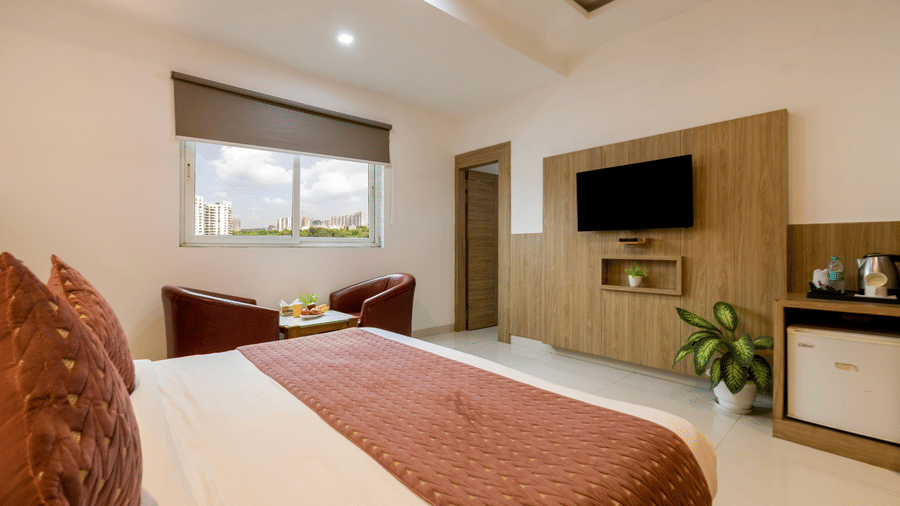 Executive Room at Hotel Corporate Suites featuring a plush bed facing the TV on the wall and a seating space by the window with daylight coming in