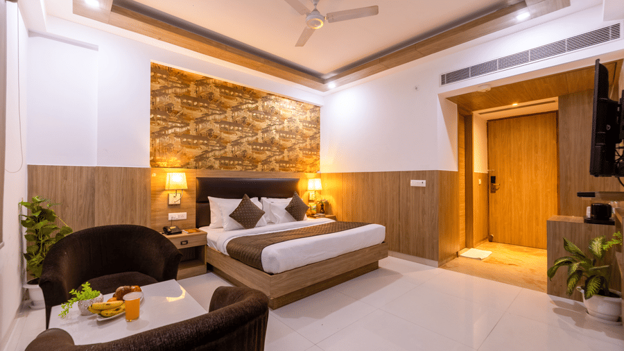 Executive Room at Hotel Corporate Suites featuring a plush bed with lamps on both sides on the nightstands and a seating space for 2 with fruits on the coffee table in the middle