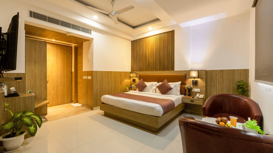 A warmly lit Executive Room at Hotel Corporate Suites featuring a plush bed facing the TV on the wall and a seating space by the window