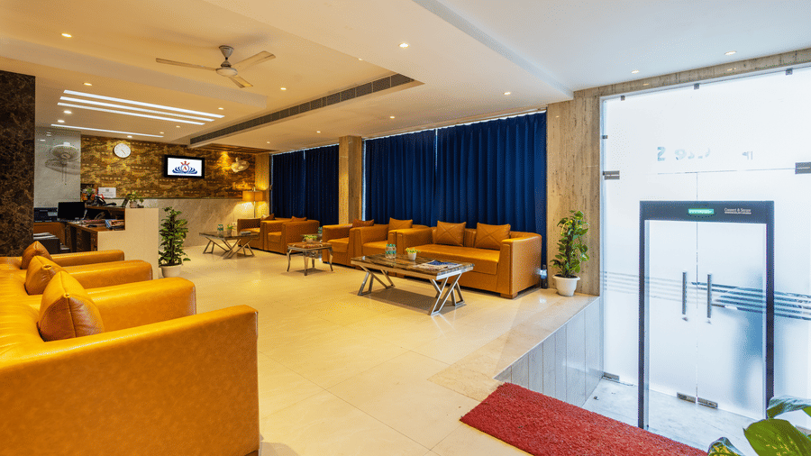 Lobby of Hotel Corporate Suites featuring plush leather seating arranged around coffee tables, illuminated by warm downlighting and complemented by royal blue curtains