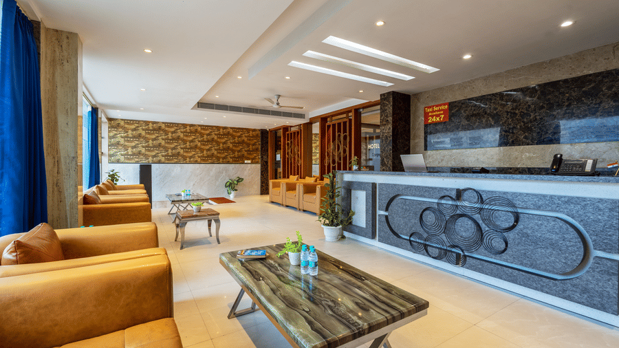 Lobby at Hotel Corporate Suites showcasing a reception desk with a marbled countertop, with a taxi service sign, ambient lighting, and sophisticated dark tiling