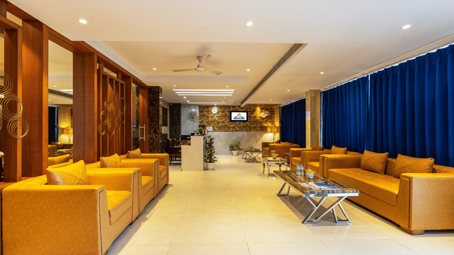 Lobby featuring plush mustard yellow sofas, elegant marble flooring, and large windows adorned with deep blue curtains at Hotel Corporate Suites