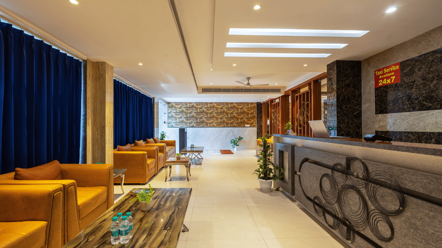 Reception area featuring plush tan leather armchairs and a polished wooden coffee table arranged against a backdrop of curtains at Hotel Corporate Suites