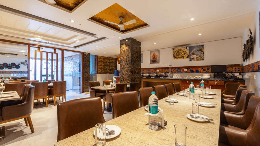 The Curry House featuring well-laid tables with sparkling glassware, brown leather chairs, and artistic wall mounted decorations under ceiling fans at Hotel Corporate Suites