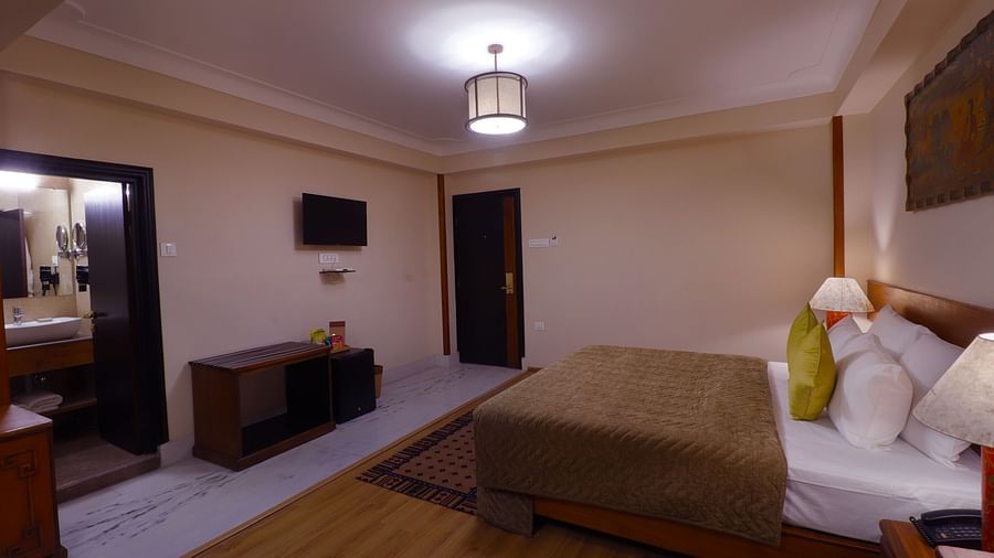 Hotel room with a bed, a dark wood dresser, a framed picture, and a doorway leading to another room -Hotel Denzong Shangrila Lords Inn