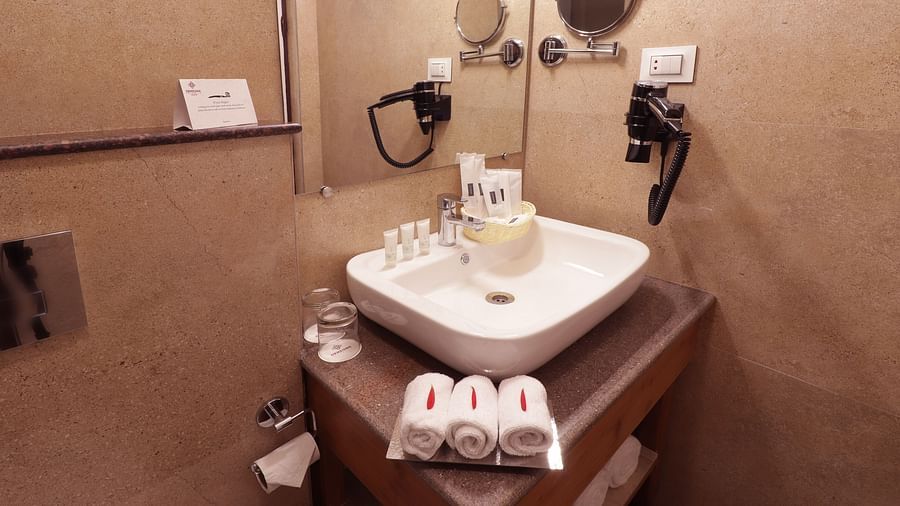 Bathroom with a modern white sink, toiletries, a mirror, and a hairdryer mounted on the wall - Hotel Denzong Shangrila Lords Inn