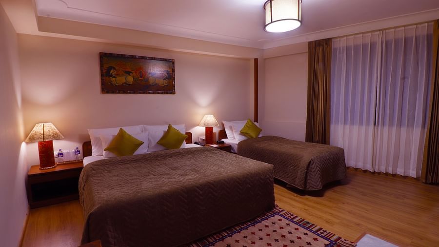 Hotel room with two beds, warm lighting, bedside lamps, artwork, and a patterned rug on the floor -Hotel Denzong Shangrila Lords Inn