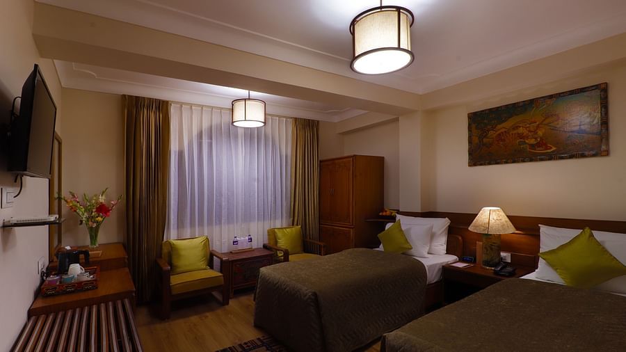 Hotel room interior with two beds, seating area with armchairs, curtains, and a central ceiling light -Hotel Denzong Shangrila Lords Inn