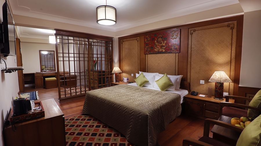 A spacious and elegant hotel room with a king-sized bed, a sitting area with a sofa and chairs, and a large window -Hotel Denzong Shangrila Lords Inn