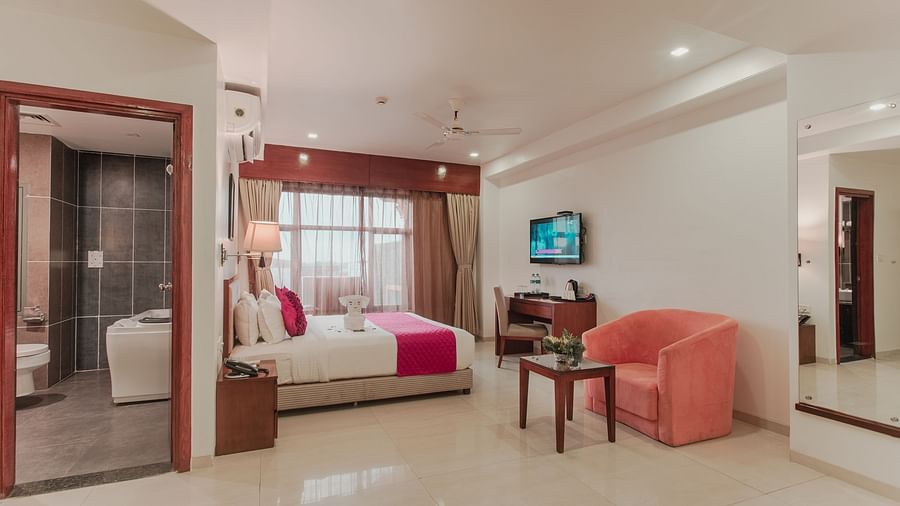 Bright hotel suite at Diamond Palace Lords Plaza with a double bed, seating area, desk, and an open bathroom view.