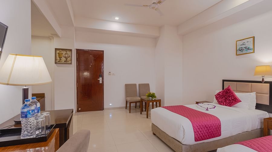 Bright hotel room at Diamond Palace Lords Plaza with twin beds featuring pink accents and a work desk area.