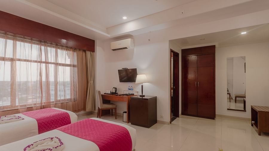 Comfortable twin room at Diamond Palace Lords Plaza with two single beds accented in pink, a work desk, and a mounted TV.