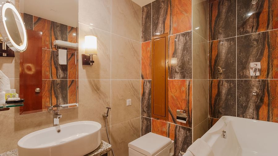 Modern bathroom at Diamond Palace Lords Plaza featuring a sink, toilet, bathtub, and uniquely patterned tiles.