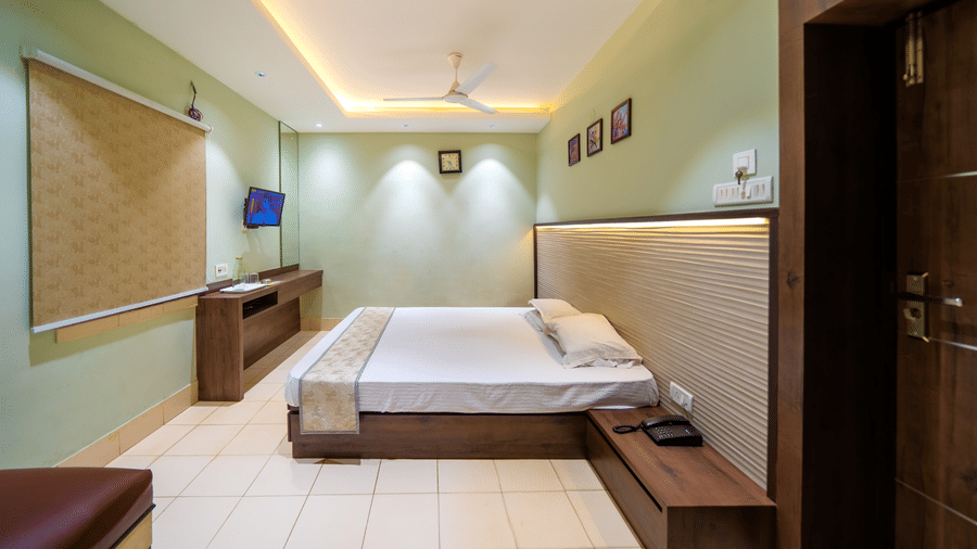 Minimalist bedroom with a double bed, ceiling lights, wall-mounted TV, and light-coloured walls – Hotel Dolphin Puri