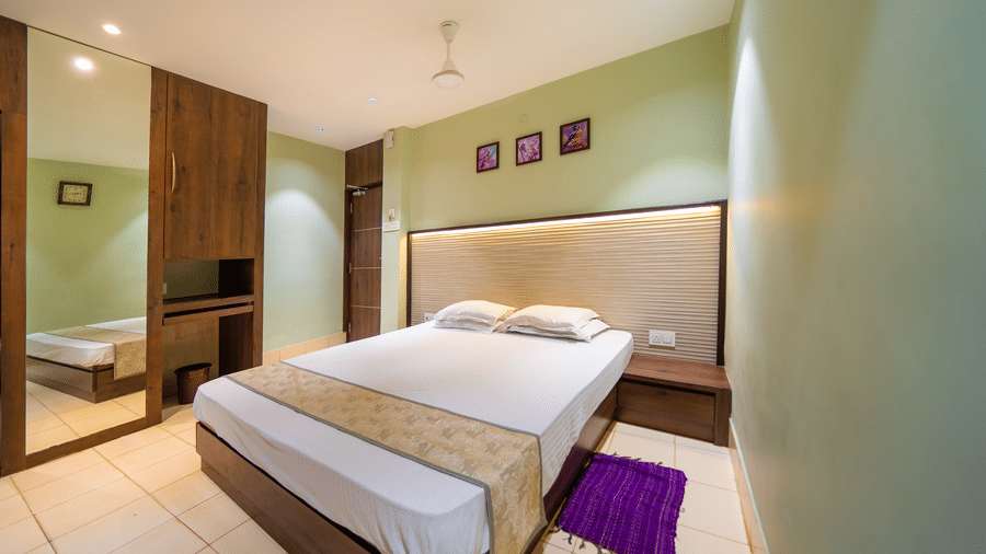 Minimalist room with double bed, wooden furniture, ceiling fan, and framed artworks above the bed – Hotel Dolphin Puri