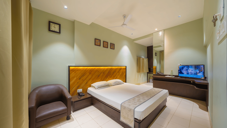 A spacious hotel bedroom featuring a double bed with a headboard, light green walls, a TV, and a leather armchair - Hotel Dolphin Puri