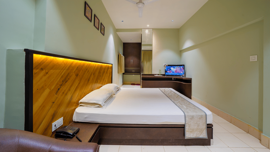 A hotel bedroom showing the double bed, modern wooden headboard, and a reflection in a large mirror - Hotel Dolphin Puri