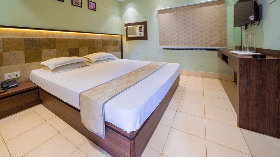 Spacious room with a double bed, wooden furniture, tiled floor, and framed artwork on the wall – Hotel Dolphin Puri