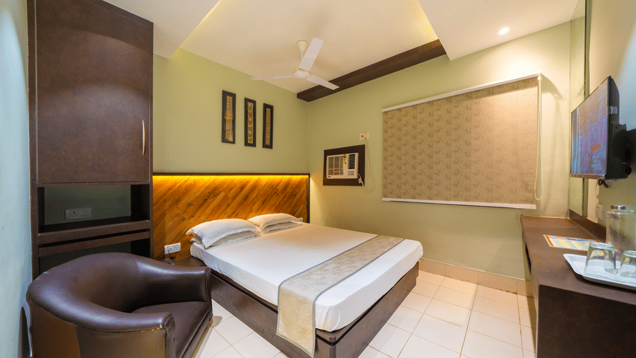 A hotel bedroom with light green walls, a double bed, a dark wood headboard, a round leather armchair, and a small desk - Hotel Dolphin Puri