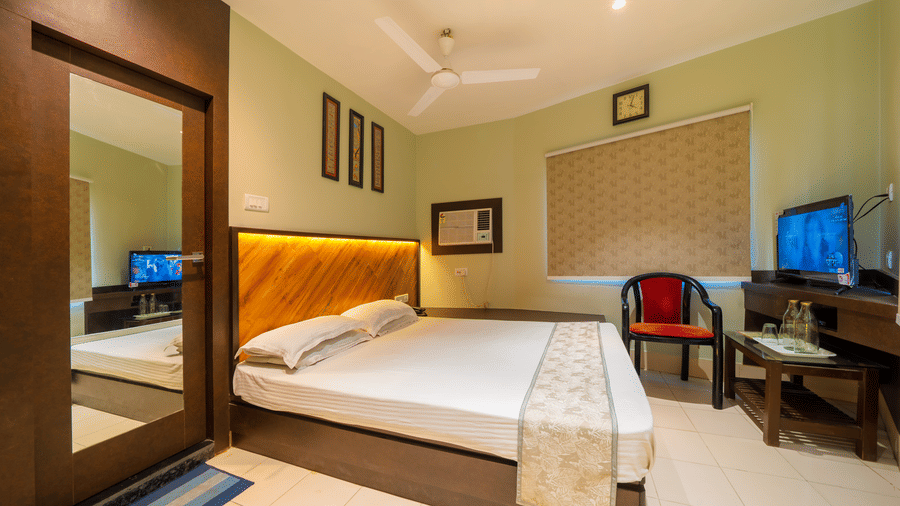 A spacious hotel bedroom showing the double bed, a wooden wardrobe with a full-length mirror, a closed blind on the window, and a TV - Hotel Dolphin Puri
