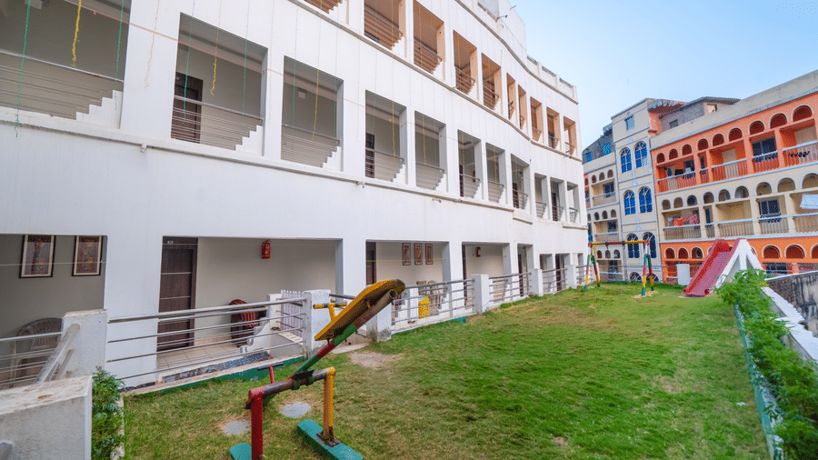 The exterior of a multi-storey, white modern hotel building surrounding a central courtyard with a green lawn and a small children's play area - Hotel Dolphin Puri