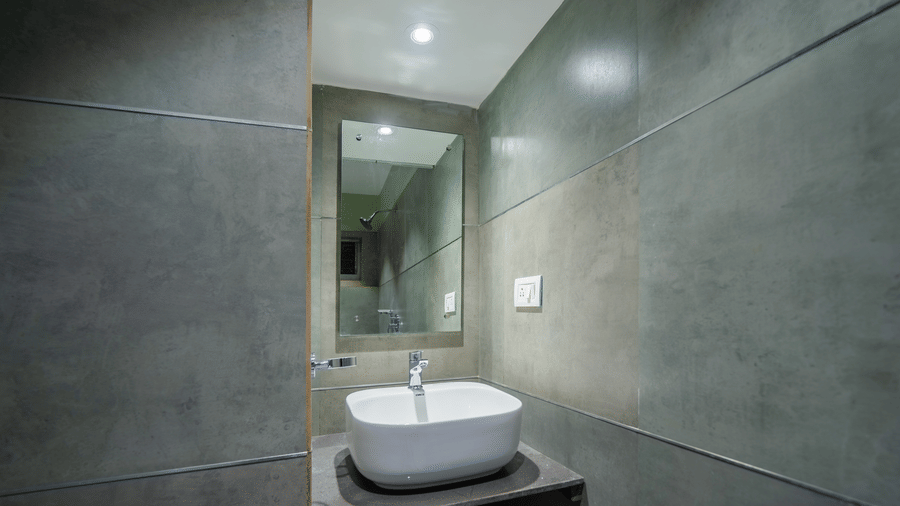 Bathroom with a washbasin, mirror, and grey tiled walls – Hotel Dolphin Puri
