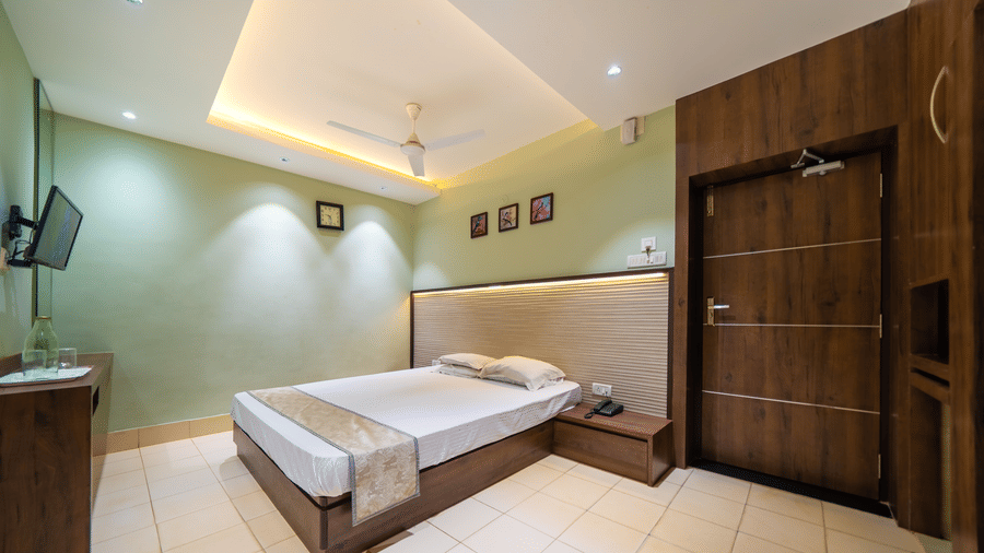 A modern hotel room with dark wood accents on the walls, a double bed, and a wall-mounted TV - Hotel Dolphin Puri