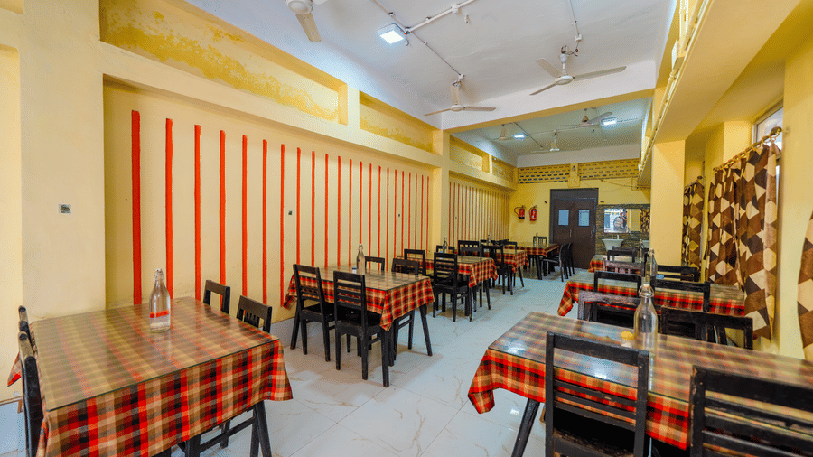 A brightly-lit, empty hotel dining hall with small tables covered in red and black checkered tablecloths and matching chairs - Hotel Dolphin Puri