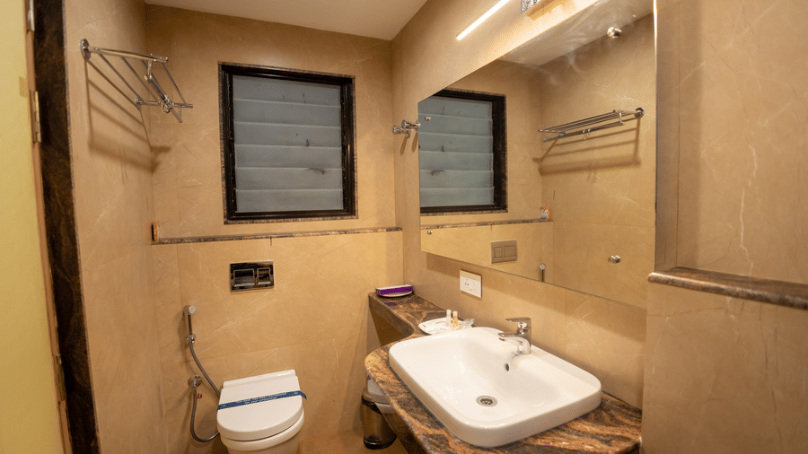 Bathroom interior with vanity mirror, countertop basin, toilet, and towel rack at Hotel Grand Sabarees Madurai.