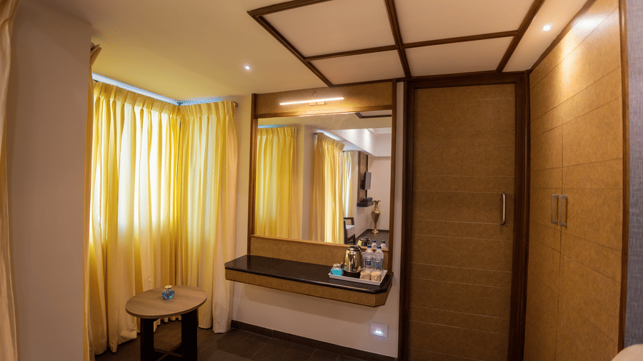 Executive Premium Room showcasing a queen bed with yellow accent linens, side table, wall-mounted TV, and window curtains at Hotel Grand Sabarees Madurai.