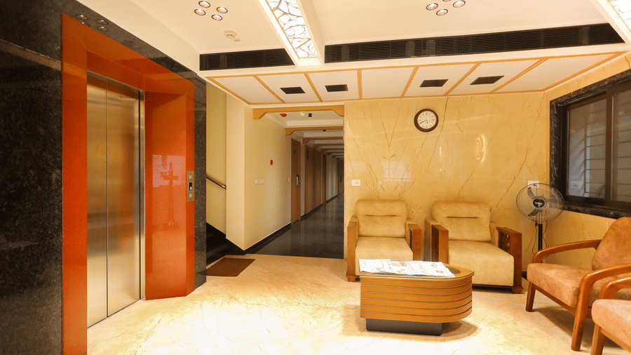 Elevator doors, corridor hallway, and comfortable armchair seating in the lobby area at Hotel Grand Sabarees Madurai.