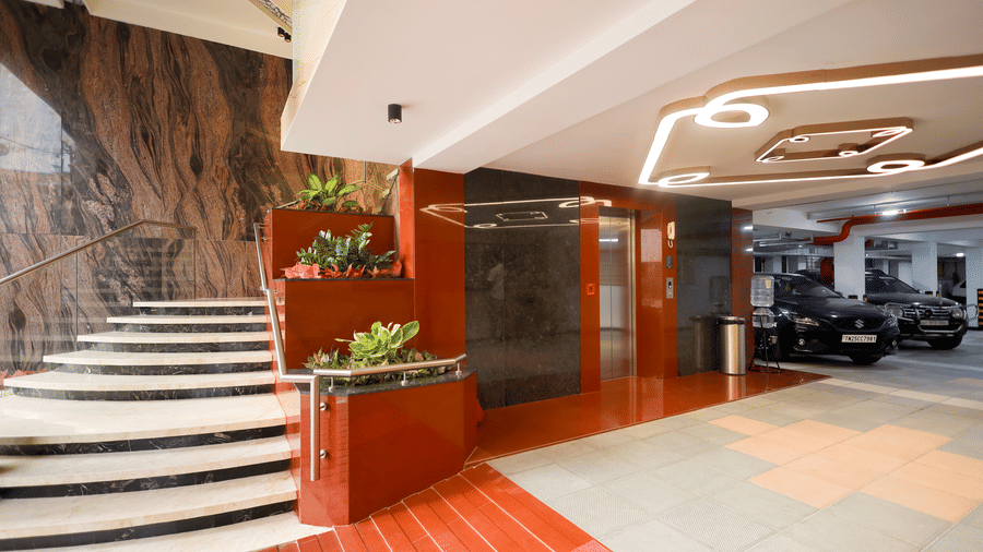 Lobby area featuring a curved marble staircase, elevator door, and indoor potted plants at Hotel Grand Sabarees Madurai.