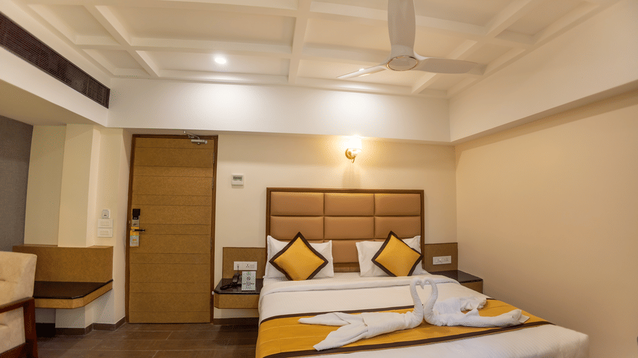 Premium oom at Hotel Grand Sabarees Madurai showing a double bed decorated with swan towel art, yellow throw pillows, and yellow bed runner.