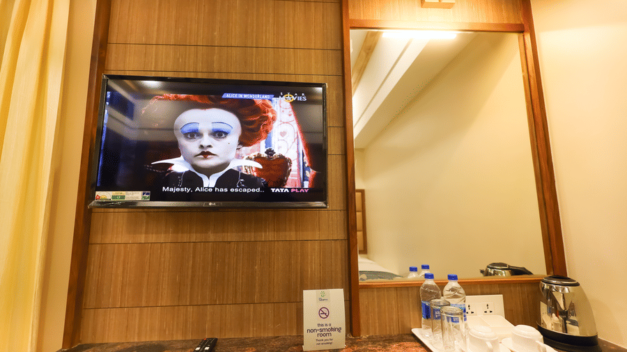 Wall-mounted Smart TV setup at Hotel Grand Sabarees Madurai alongside a vanity mirror, complimentary mineral water bottles, and tea-coffee maker.