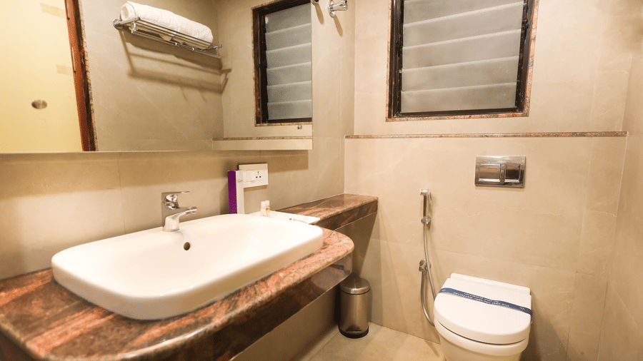 Bathroom featuring a countertop washbasin, mirror, frosted glass window, towel rack, and modern toilet at Hotel Grand Sabarees Madurai.