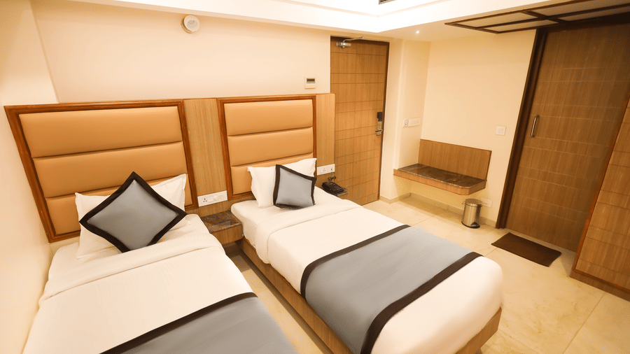 Executive Twin Room at Hotel Grand Sabarees Madurai featuring two single beds, padded headboards, bedside nightstand, telephone, and wooden wardrobe.
