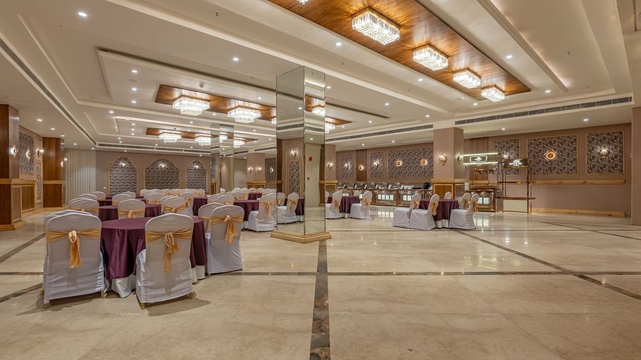 Banquet hall at Hotel Highway King, Bagru, featuring decorated chairs, round tables, mirrored walls, and ceiling lights.