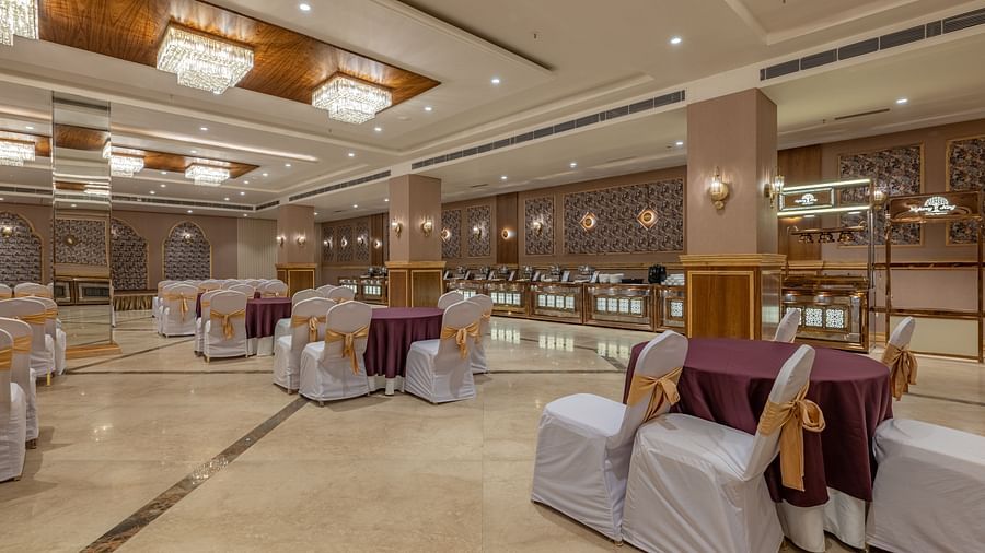 Banquet hall at Hotel Highway King, Bagru, with decorated chairs, chandeliers, wood-paneled walls, and mirrored sections.