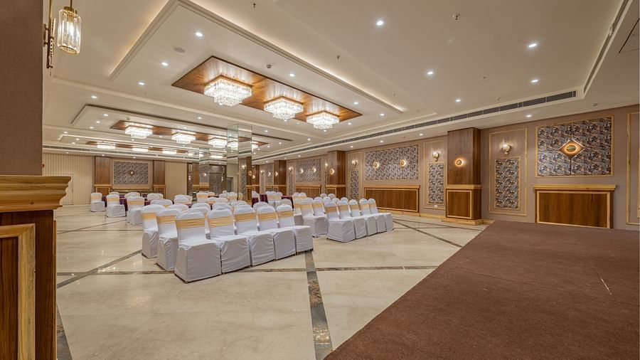 Conference hall at Hotel Highway King, Bagru, with arranged chairs, decorative ceiling, and wood-paneled walls.