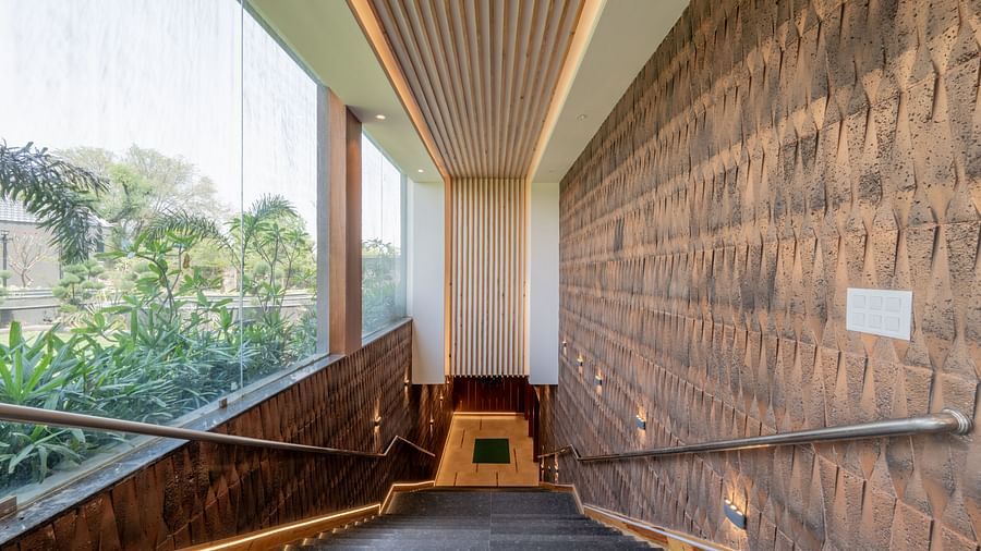 Staircase at Hotel Highway King, Bagru, with textured walls and a large window overlooking the garden area.