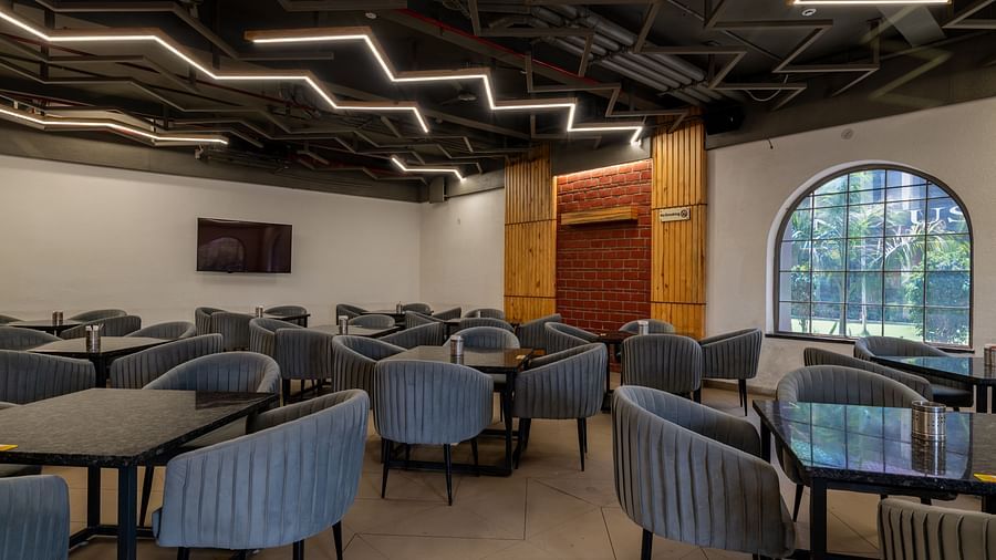 Indoor dining area at Hotel Highway King, Bagru, with multiple tables, upholstered chairs, and modern ceiling lighting.