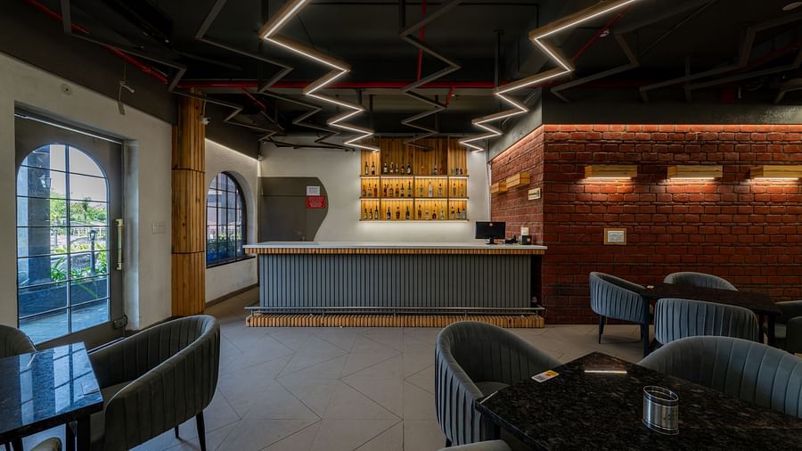 Bar area at Hotel Highway King, Bagru, with modern seating, illuminated ceiling design, and brick accent walls.