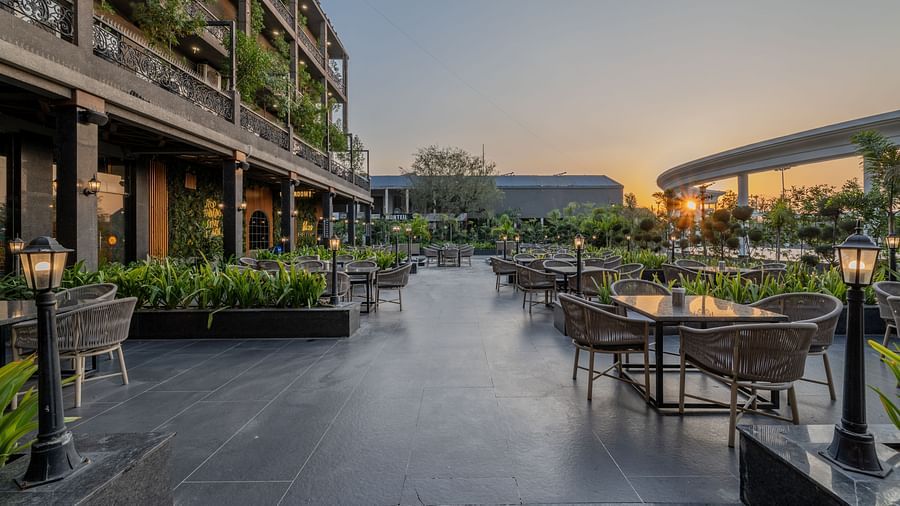 Outdoor seating area at Hotel Highway King, Bagru, with tables, chairs, greenery, and the hotel building in the background.